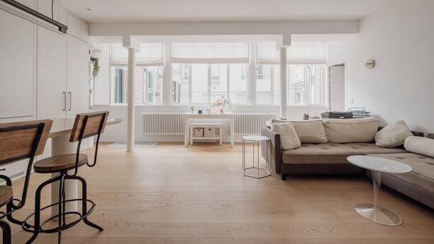 Une cuisine moderne avec des meubles blancs, un coin repas avec des chaises en bois, une table blanche et un canapé beige.