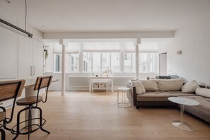 Eine moderne Küche mit weißen Schränken, einem Essbereich mit Holzsesseln, einem weißen Tisch und einem beigen Sofa.