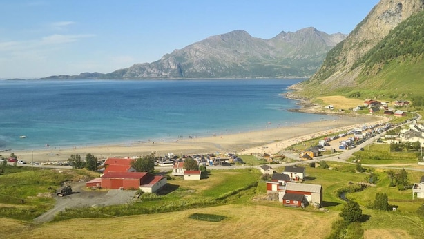 A coastal town with a beach, houses, and mountains in the background.