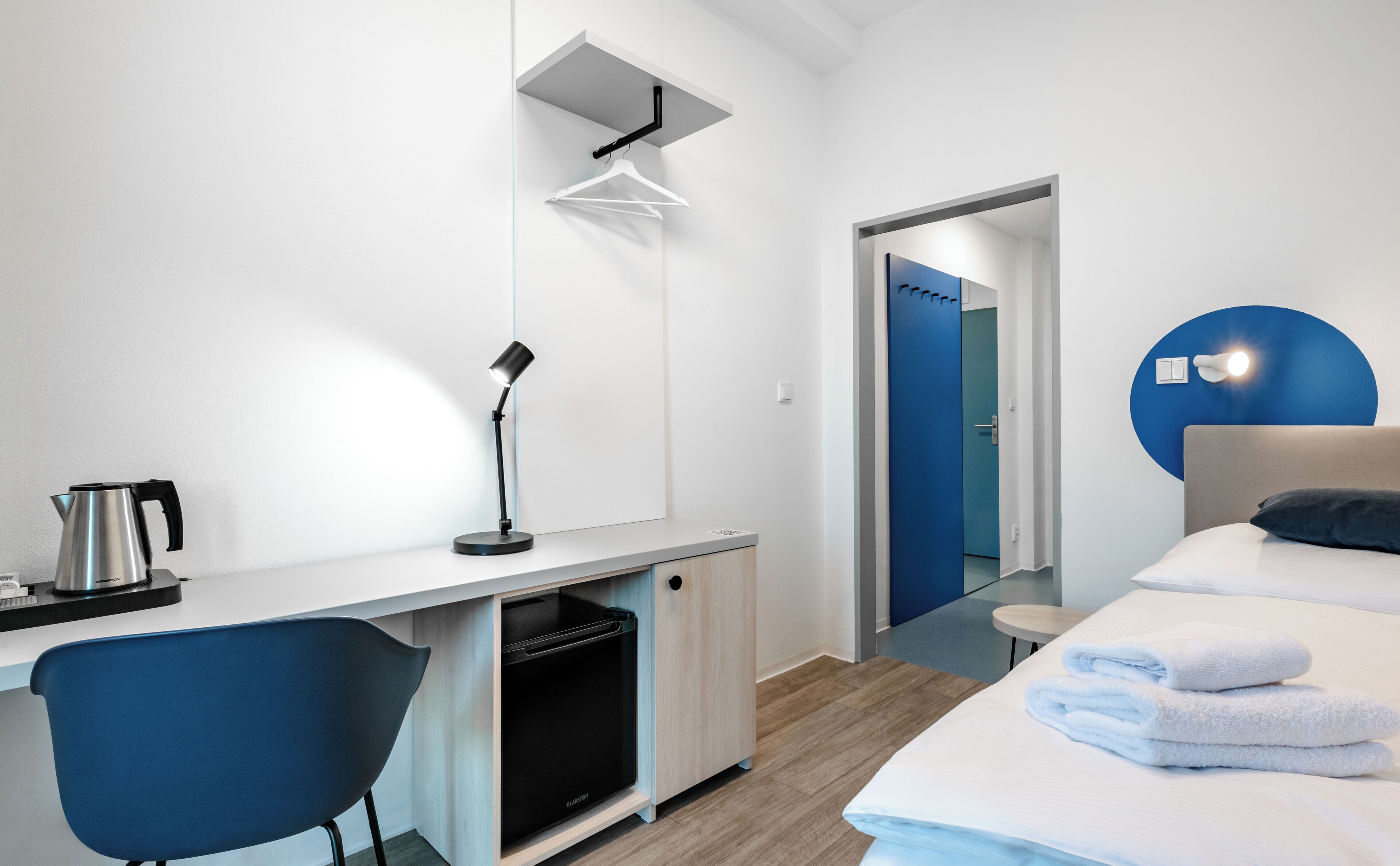 Et moderne hotelværelse med skrivebord, stol, seng og en blå accentvæg.