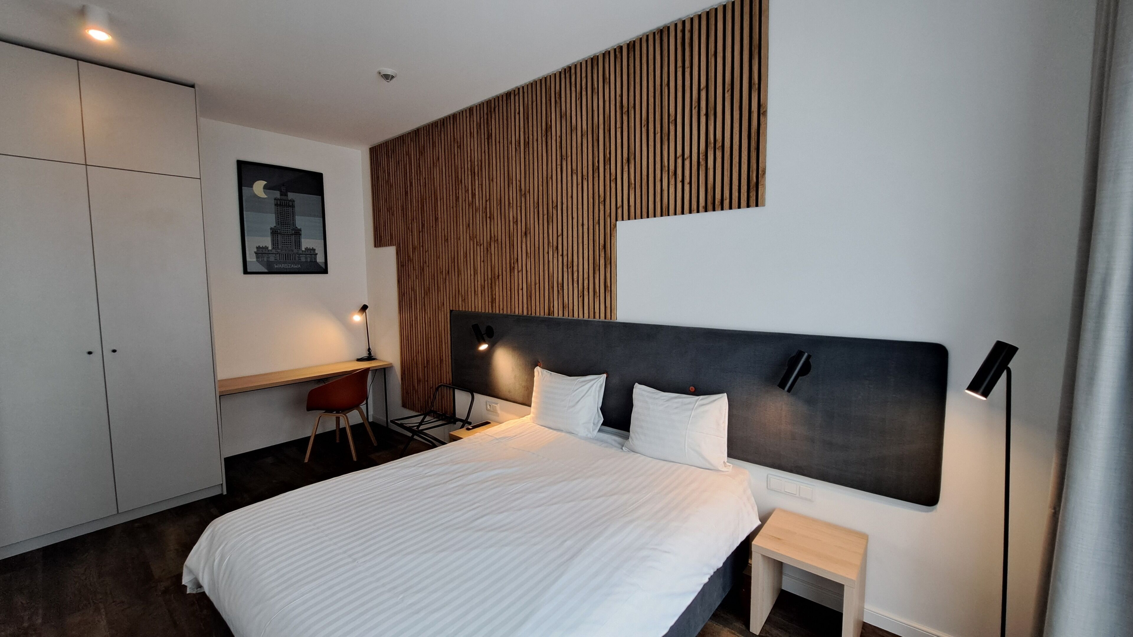 A modern hotel room with a large bed, a desk, and a chair.