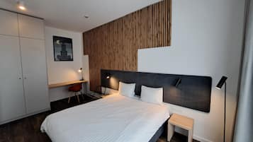 A modern hotel room with a large bed, a desk, and a chair.