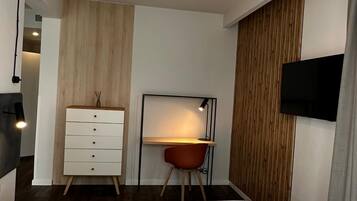 A modern bedroom with a bed, a desk, a chair, a dresser, and a TV mounted on the wall.