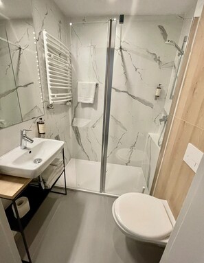 Ein modernes Badezimmer mit einer Duschkabine aus Glas, einem weißen Waschbecken und einer Toilette.