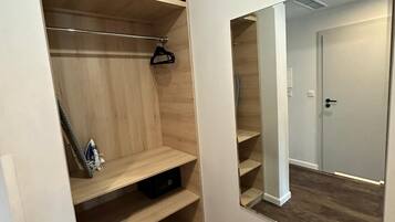 A walk-in closet with wooden shelves and a hanging rod, a small ironing board, and a mirror on the wall.