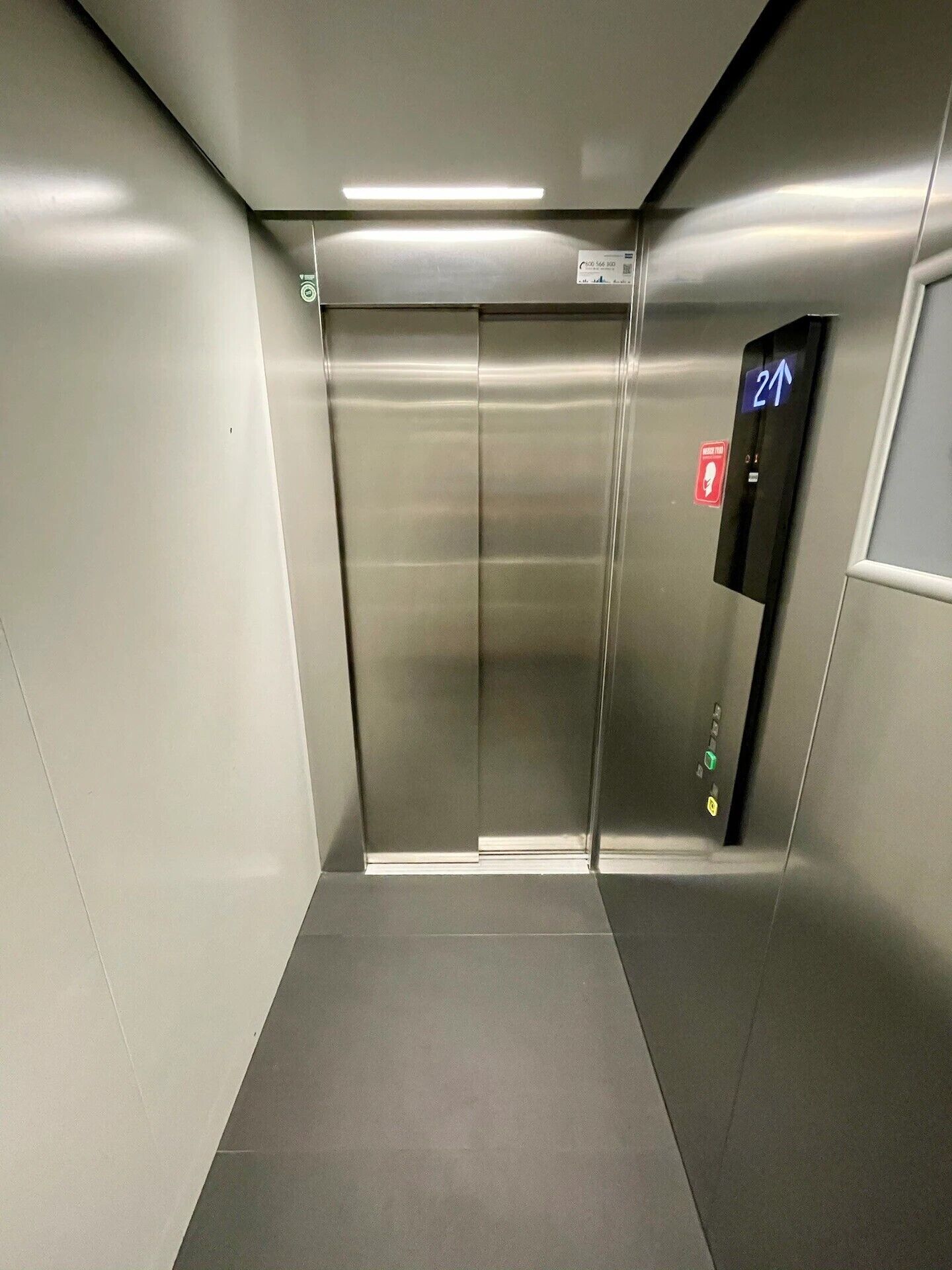 An elevator with metallic doors, a digital display, and a red emergency exit sign.