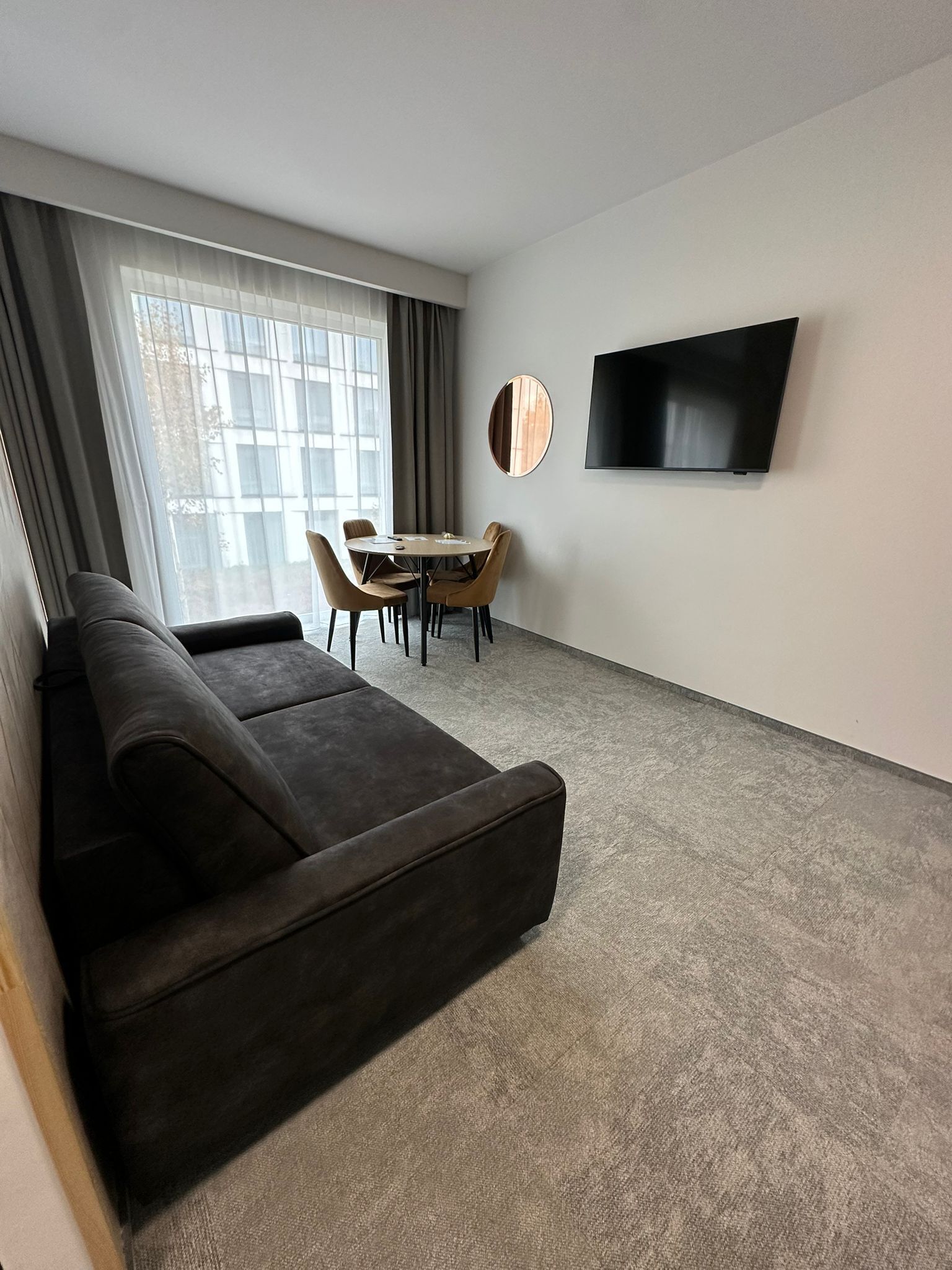 A modern living room with a dark sofa, a round coffee table, and a flat-screen TV mounted on the wall.