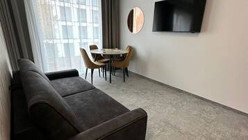 A modern living room with a dark sofa, a round coffee table, and a flat-screen TV mounted on the wall.