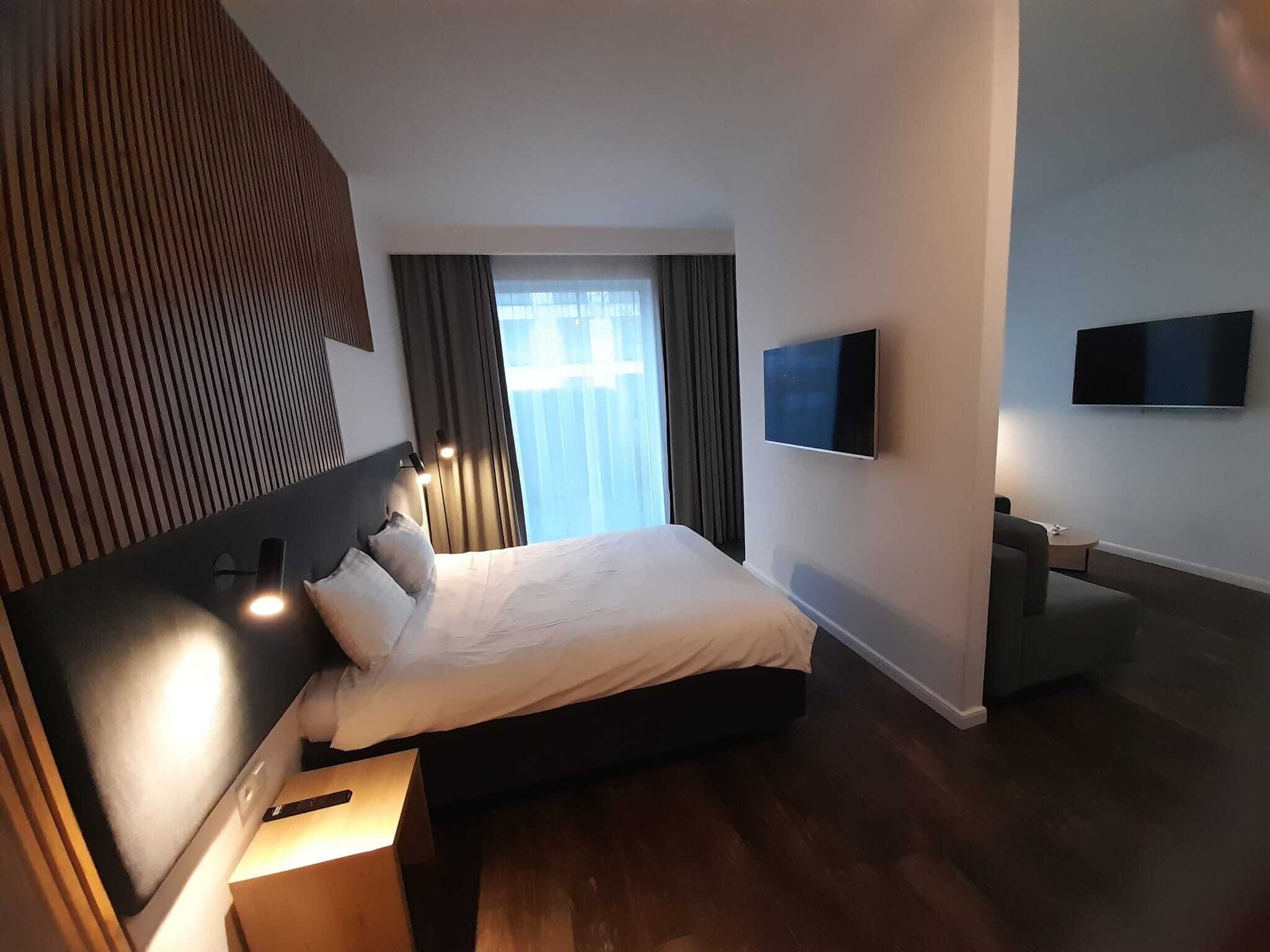 A modern hotel room with a large bed, a flat-screen TV, and a wooden floor.