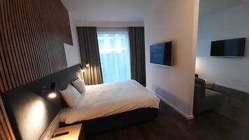 A modern hotel room with a large bed, a flat-screen TV, and a wooden floor.