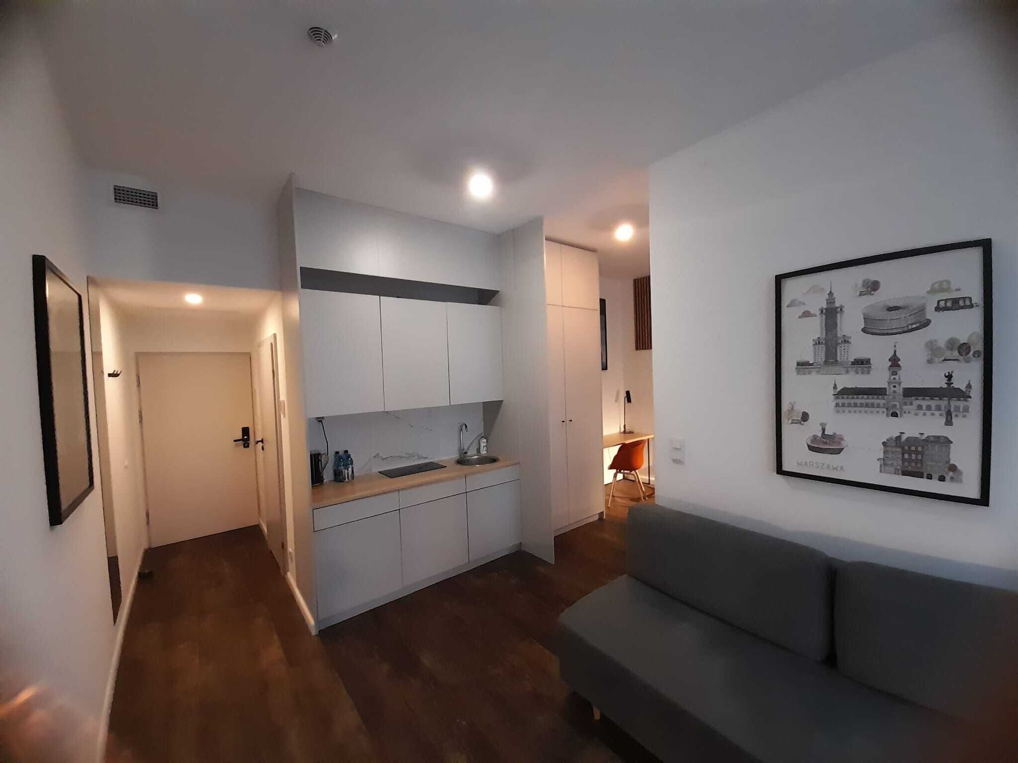 A modern kitchen with white cabinets, a wooden countertop, and a sink. There is a framed picture of Warsaw on the wall.