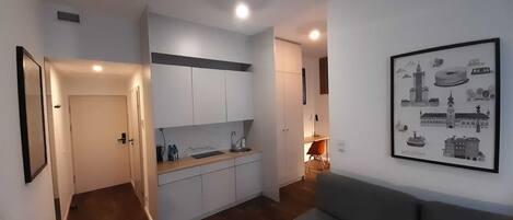 A modern kitchen with white cabinets, a wooden countertop, and a sink. There is a framed picture of Warsaw on the wall.