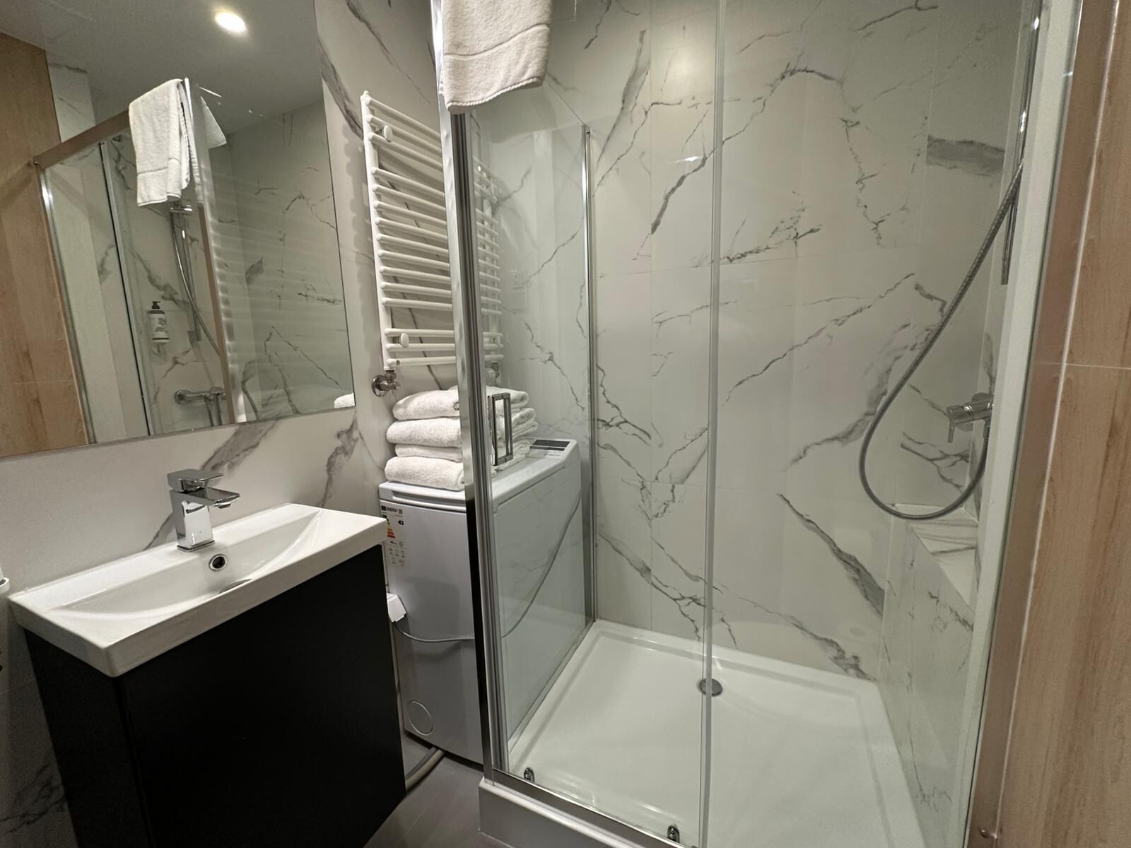 Un baño moderno con ducha envuelta en vidrio, tocador con lavamanos y perchero para toallas.