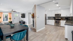 A modern kitchen with white cabinets, stainless steel appliances, and a dark wooden dining table with teal chairs. - BackyardOasis - FamilyRetreat Villa - HeatedPool (Phoenix)