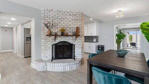 A modern kitchen with a white brick fireplace, a dining area with teal chairs, and a view of the outdoors. - BackyardOasis - FamilyRetreat Villa - HeatedPool (Phoenix)