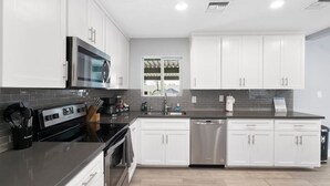 A modern kitchen with white cabinets, a stainless steel dishwasher, and a black countertop. - BackyardOasis - FamilyRetreat Villa - HeatedPool (Phoenix)