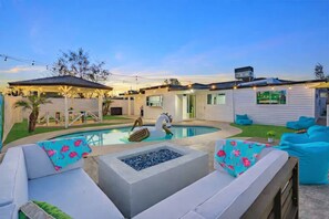 A backyard with a swimming pool, outdoor seating, and a covered patio area.