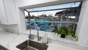 A modern kitchen with a stainless steel sink, a window overlooking a pool, and a potted plant on the windowsill. - The No Bad Days Villa - Family Retreat -Central (Phoenix)