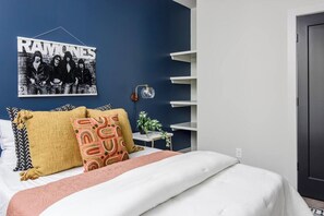 A bedroom with a bed, pillows, a wall-mounted picture, a bedside table, and a lamp.