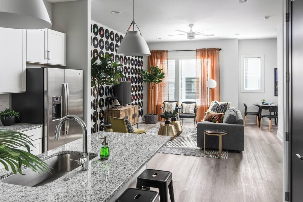 A modern kitchen with a built-in refrigerator, a granite countertop, and a sink. There is a dining area with a sofa and a small table.