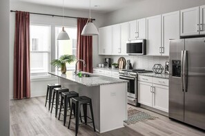 A modern kitchen with white cabinets, stainless steel appliances, a central island with stools, and pendant lighting. - House of Many Records - Brand New Spacious Luxury (Nashville)