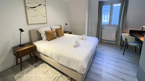 Habitació d'hotel amb un llit gran, una taula de treball, una cadira, una finestra amb cortines i un quadre a la paret.