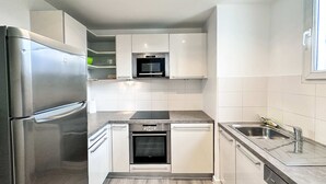 Cuina compacta amb armaris blancs, nevera d'acer inoxidable, forn integrat i rentaplats.
