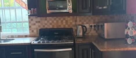 Una cocina con gabinetes oscuros, microondas, estufa y cafetera.