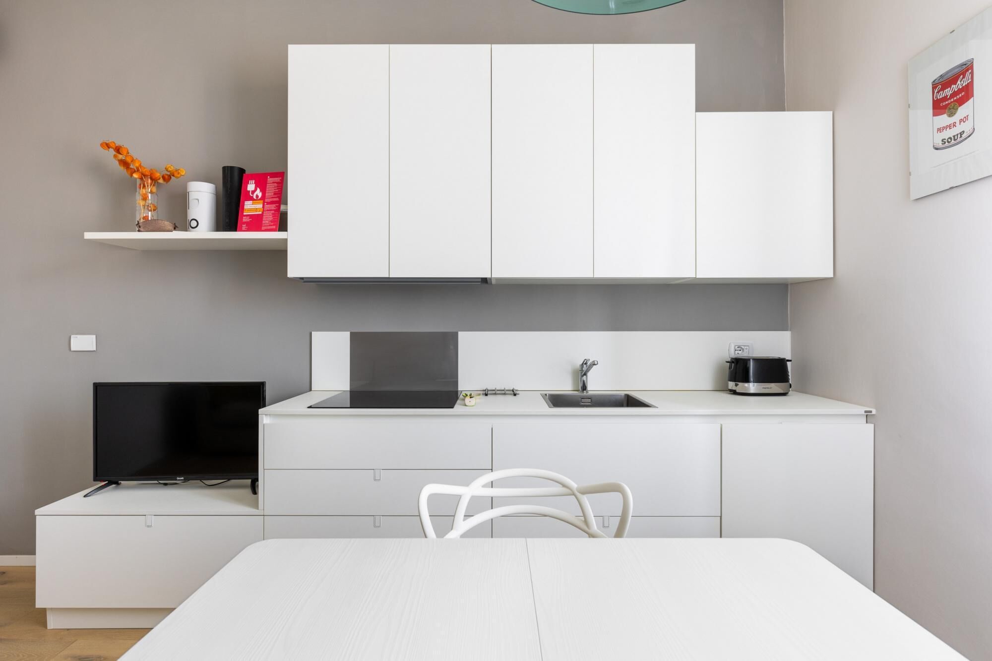 Cocina moderna con armarios blancos, una estufa negra, un fregadero y una mesa de comedor con una silla blanca.
