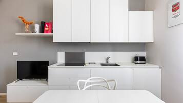 Cocina moderna con armarios blancos, una estufa negra, un fregadero y una mesa de comedor con una silla blanca.