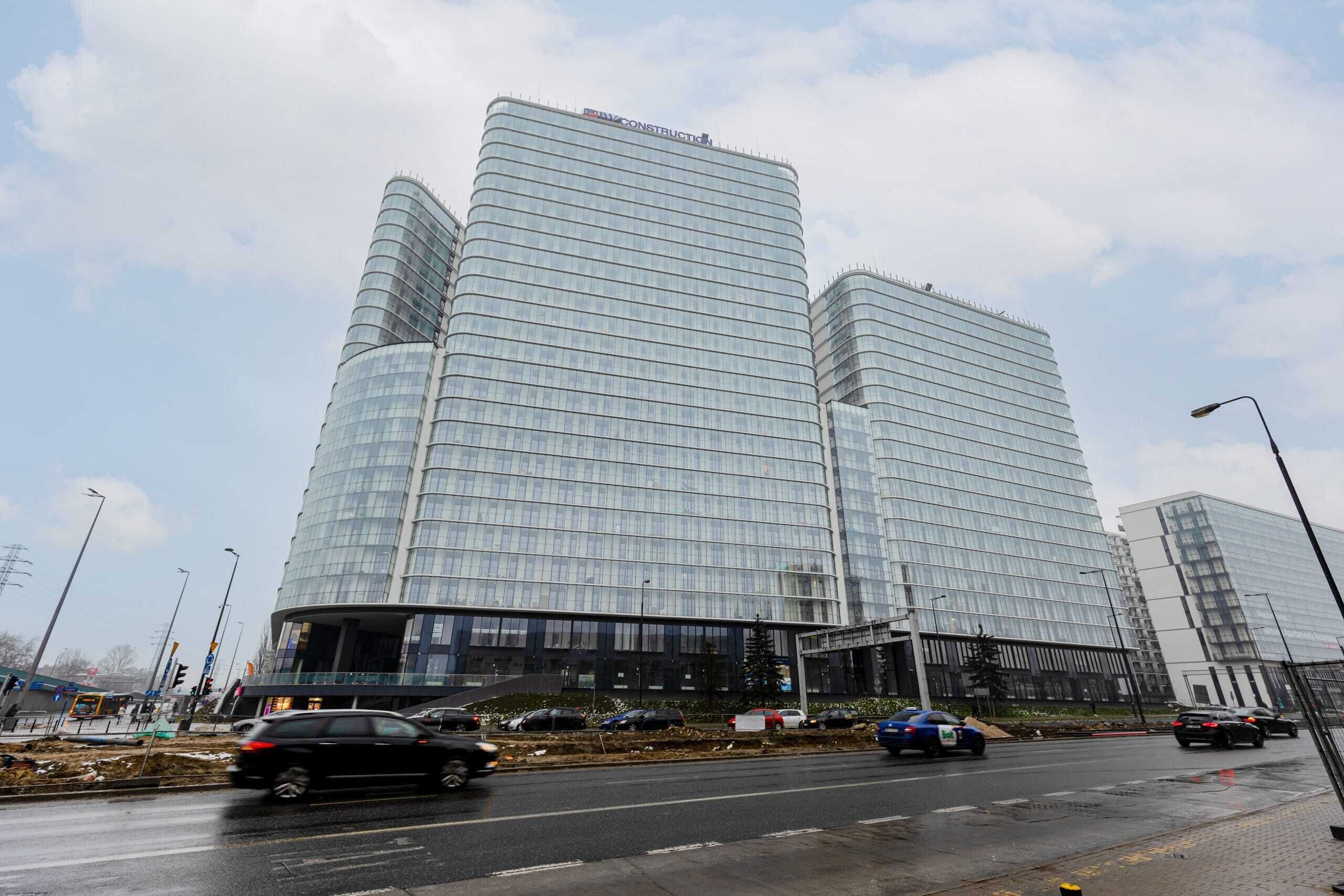 A modern glass building with a curved facade and a sign reading "CONSTRUCTION" at the top.