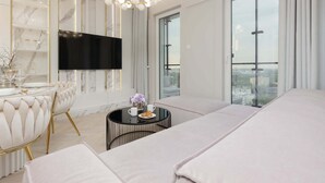 A modern hotel room with a large bed, a TV, a round table with a vase, and a balcony with a city view.