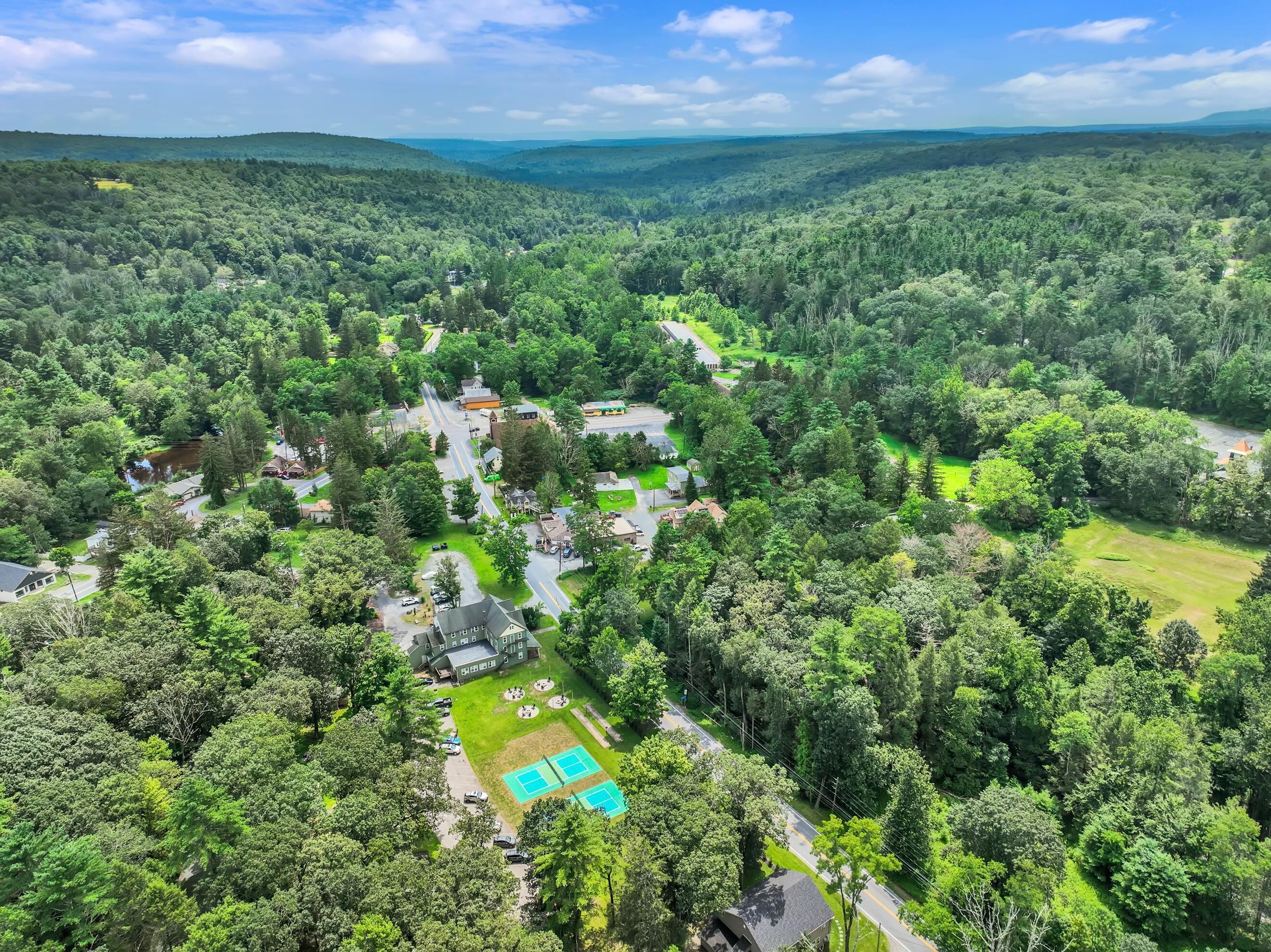 A residential area with a large house, tennis courts, and a surrounding forested landscape.