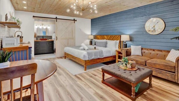 A cozy bedroom with a wooden ceiling, a bed with white linens, a blue wall, and a clock.