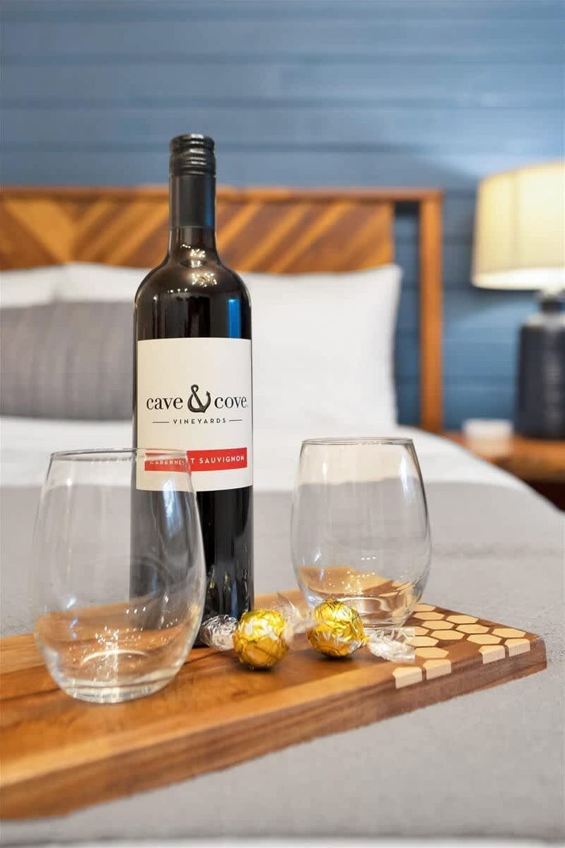 A bottle of Cave & Cove Cabernet Sauvignon on a wooden tray with two empty glasses and two wrapped chocolates.