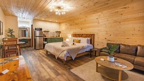Una cabana de fusta acollidora amb un llit, un sofà, una taula de dinar i una cuina.