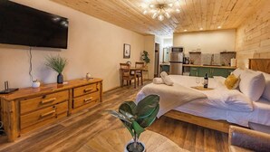 Habitació acollidora amb un llit, un taulell de fusta, televisió i una cuineta.