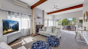 Una sala de estar moderna con chimenea, un sofá, un televisor y un comedor con asientos exteriores.