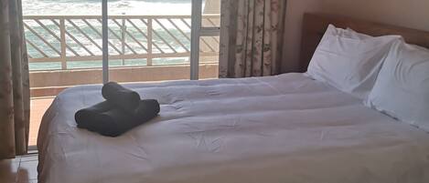 A hotel room with a large bed, a view of the ocean, and a balcony with a railing.