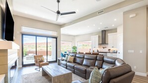 A spacious living room with a large leather sectional sofa, a coffee table, and a TV. There is a sliding glass door leading to a patio with a view of the desert. - SunChaser 2 Bed 2 bath Dog Friendly Private Home, Hot Tub, EV Charger (Washington)