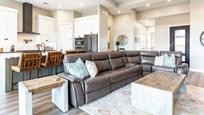 A modern living room with a sectional sofa, wooden coffee table, and a kitchen area with white cabinets and a stainless steel refrigerator. - SunChaser 2 Bed 2 bath Dog Friendly Private Home, Hot Tub, EV Charger (Washington)