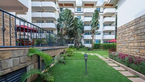 A courtyard with a stone wall, a metal railing, and a well-maintained lawn. - Roma Courts Serviced Apartments (Nairobi)