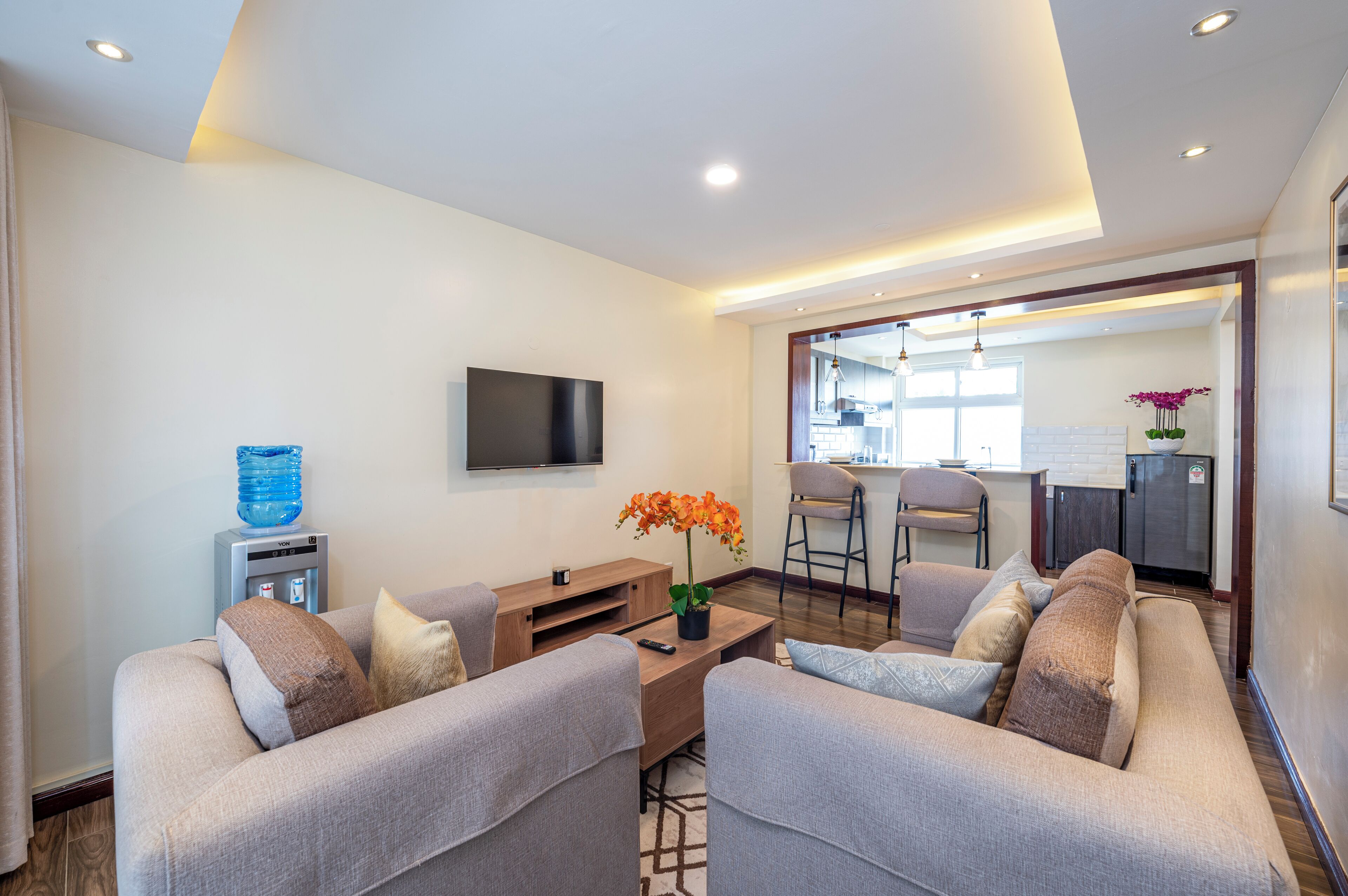 A modern living room with two sofas, a coffee table, a TV, and a water dispenser.