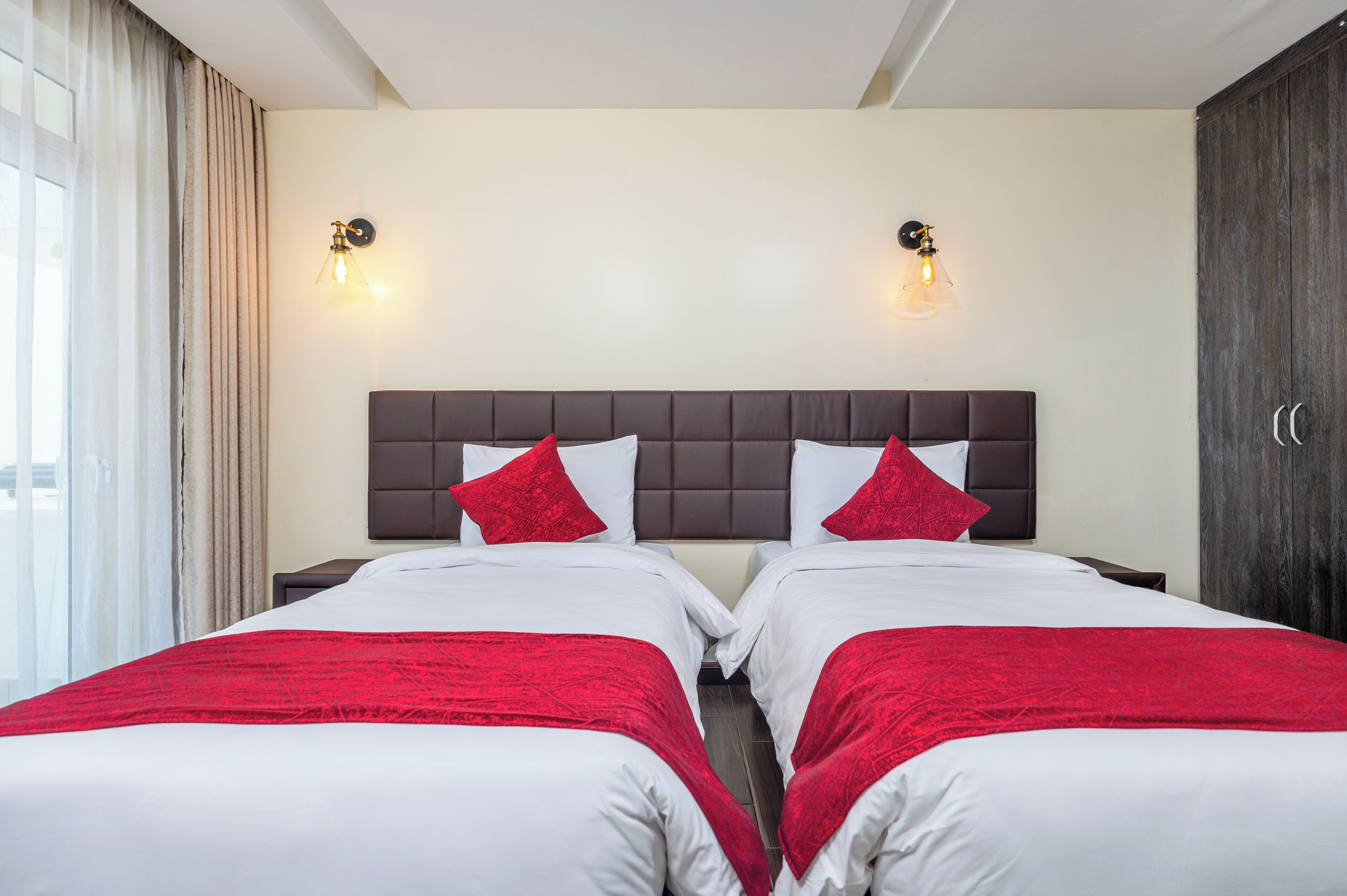 Een hotelkamer met twee bedden, elk voorzien van witte beddengoed en rode accenten, een donker hoofdeinde en wandlampen.