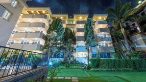 A multi-story hotel with balconies, a well-maintained garden, and a night sky. - Roma Courts Serviced Apartments (Nairobi)
