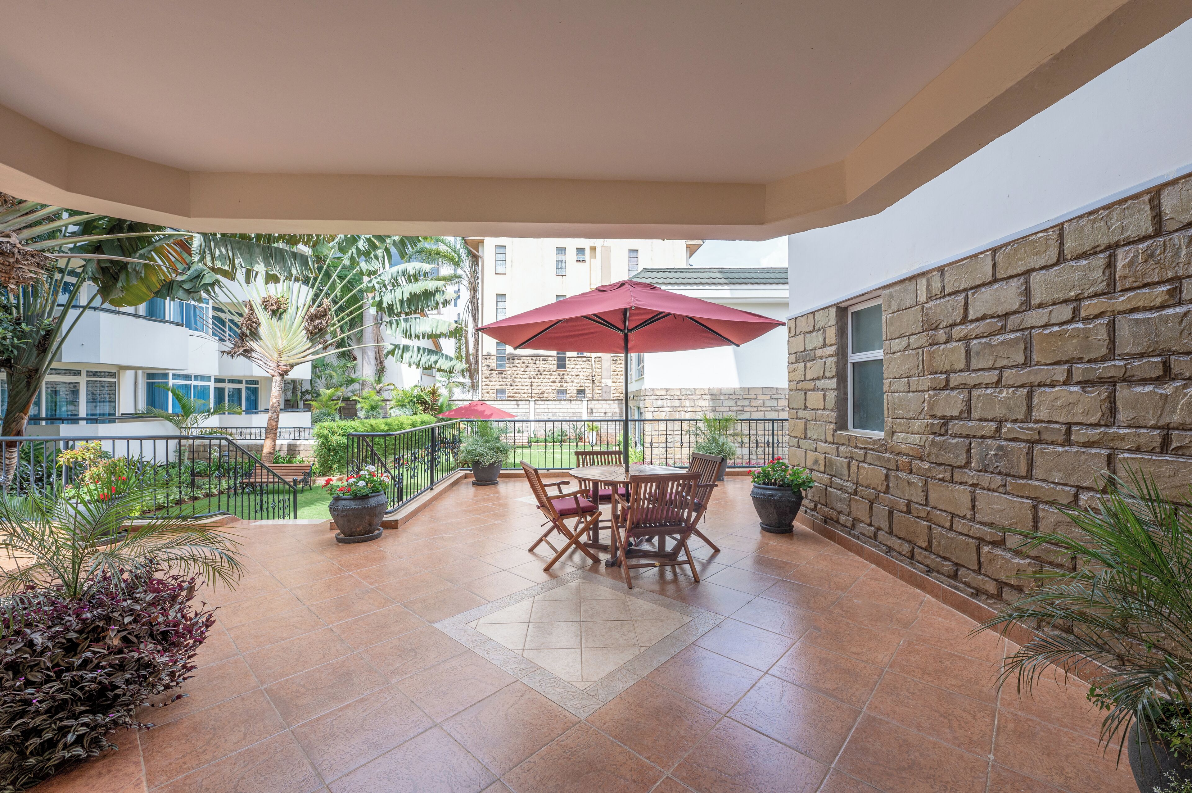 A covered patio area with a table and chairs, surrounded by potted plants and a stone wall.