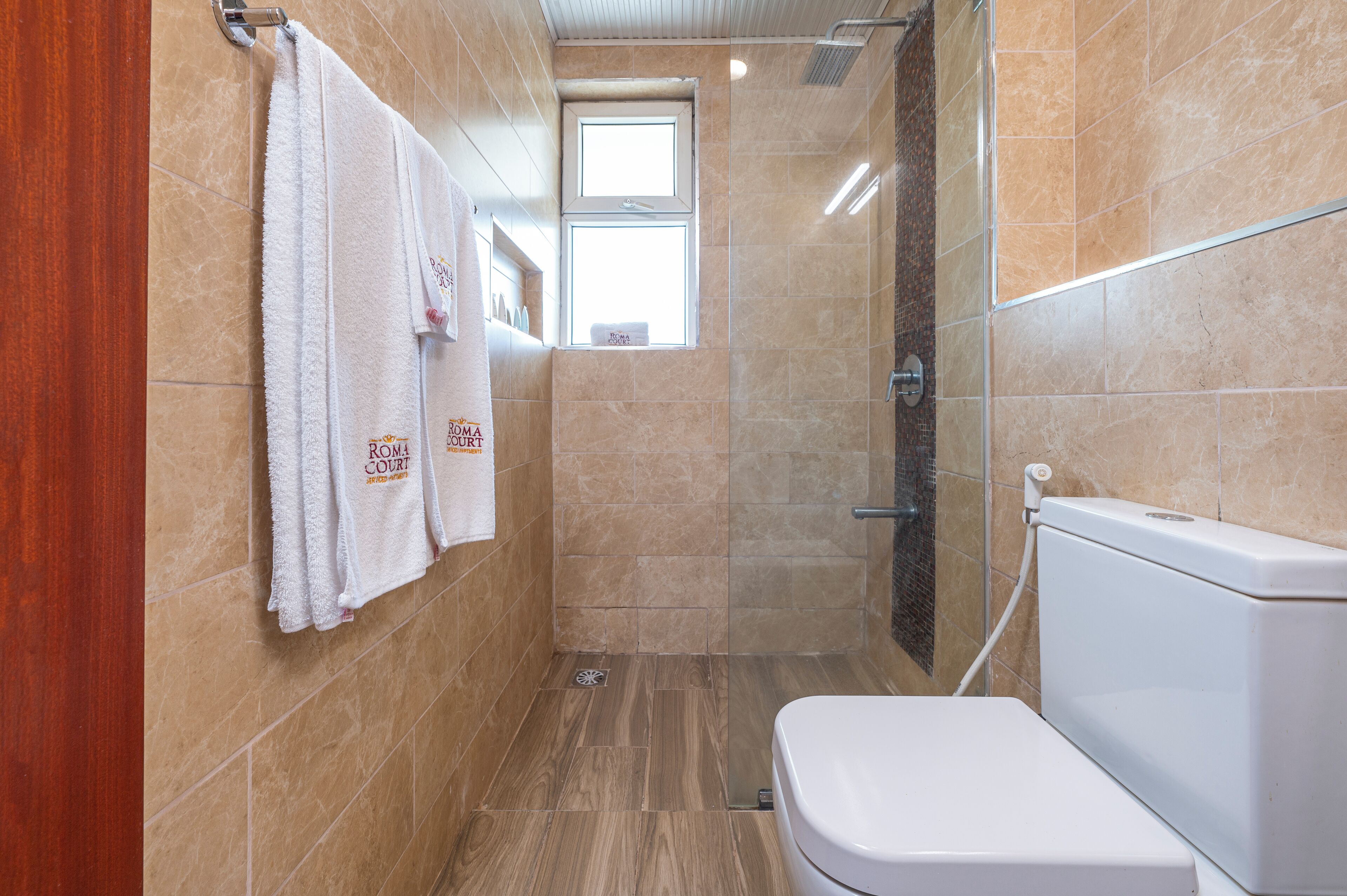 Een badkamer met een toilet, een douche met glazen deuren en twee handdoeken aan de muur.