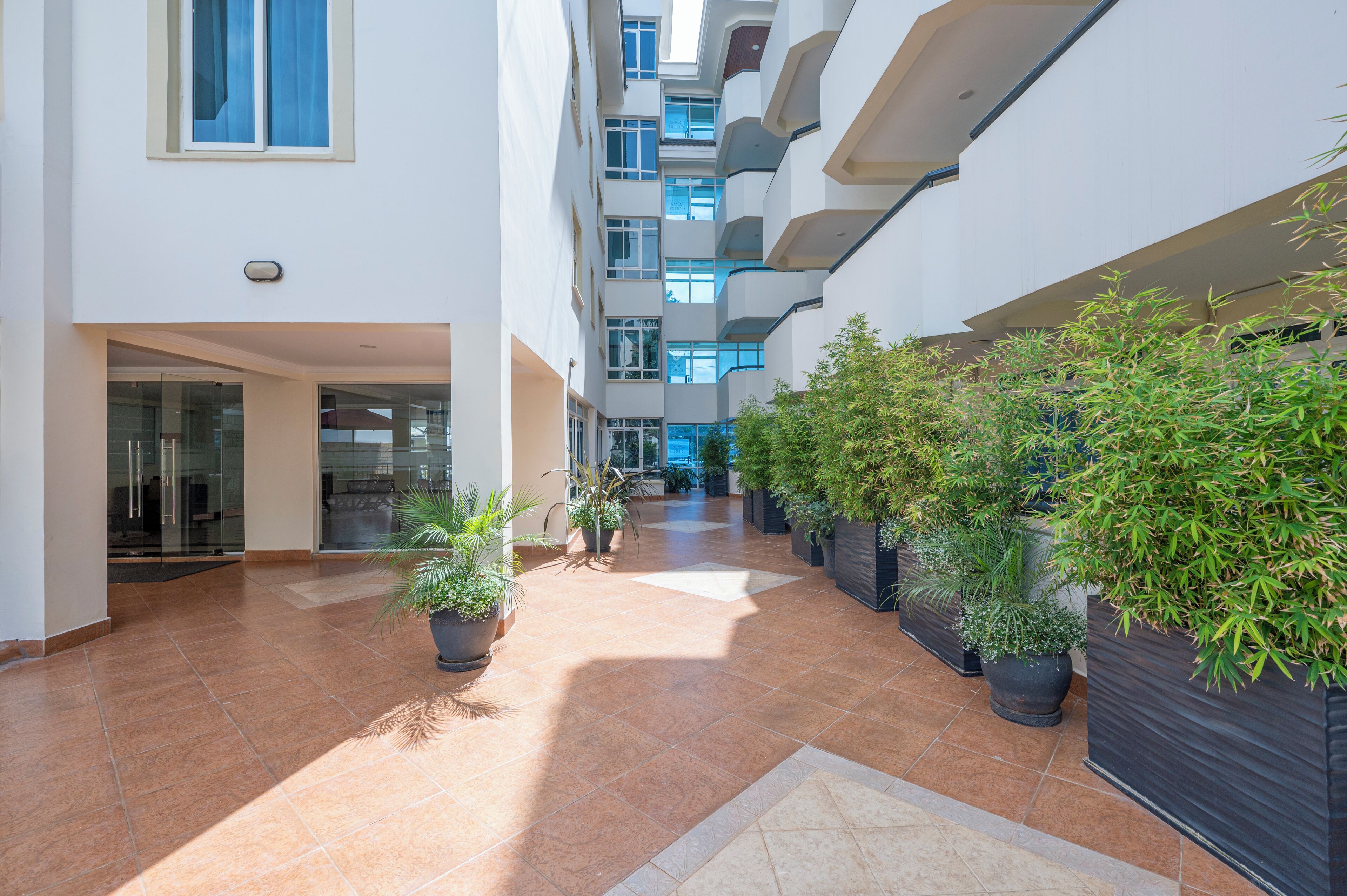 A modern indoor corridor with multiple floors, potted plants, and glass doors leading to rooms.