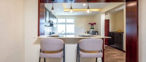 A kitchen with two bar stools, a central island, pendant lighting, and a view into the dining area.