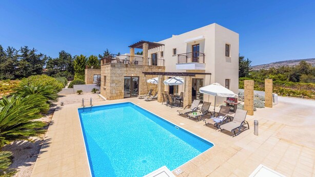 A modern two-story house with a swimming pool, outdoor seating, and a view of the surrounding landscape. - Villa Anthia (Pegeia)